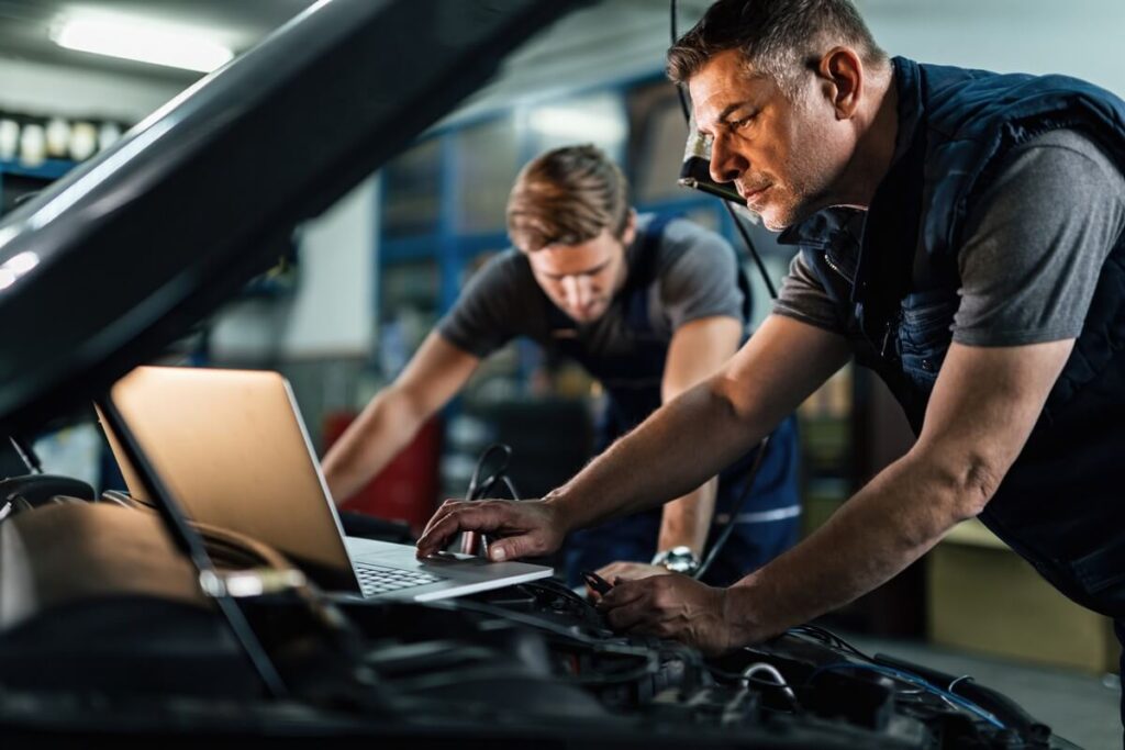 mid adult mechanic using computer doing car diagnostic with his coworker auto repair shop